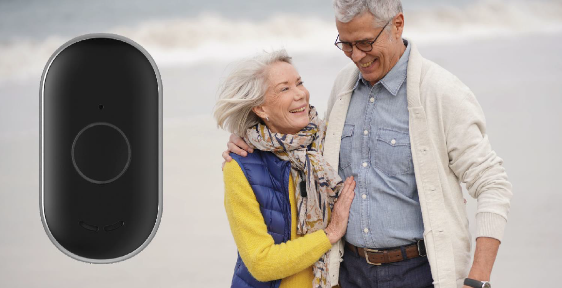 Couple de personnes âgées souriantes portant le dispositif de surveillance de chutes GisiguLink sur la plage.